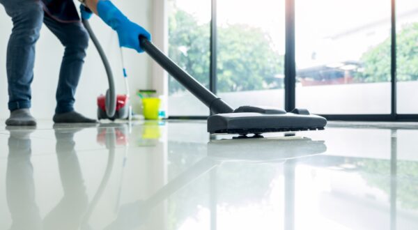 Young attractive man is cleaning vacuum commercial cleaning equipment on floor at home helping wife